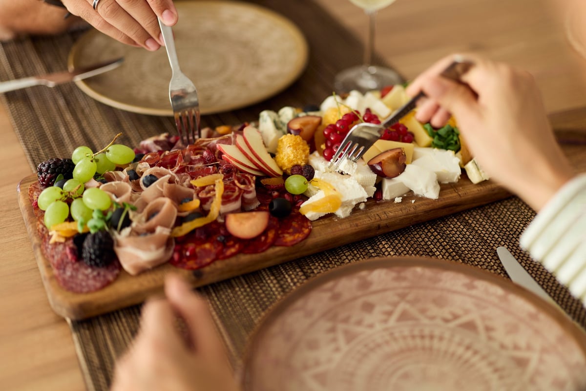 Hands reaching across a sharing platter of cheese, meats and fruit